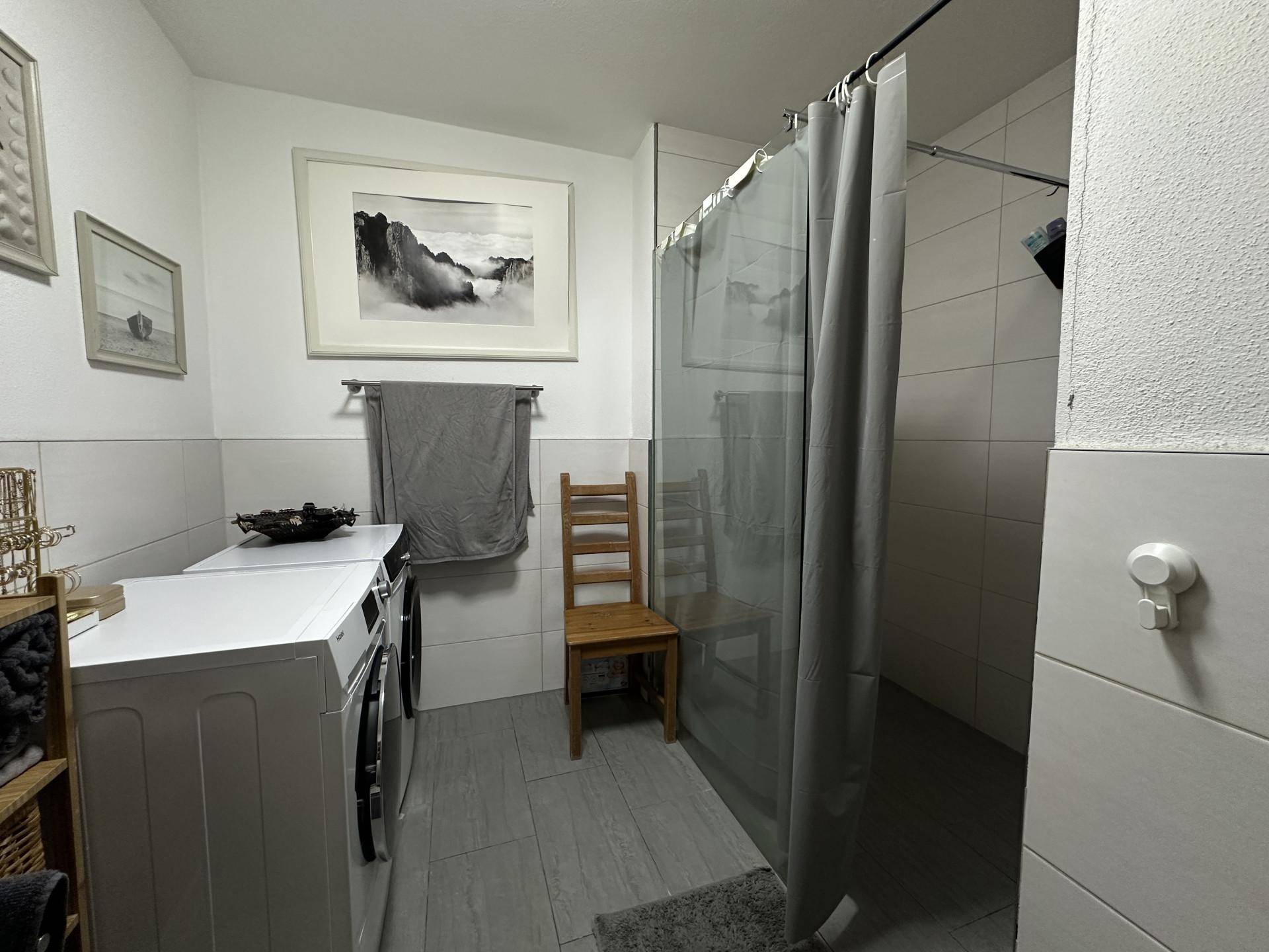 Funktionales Badezimmer mit einer geräumigen Dusche und integrierten Waschmaschinen für zusätzlichen Komfort.