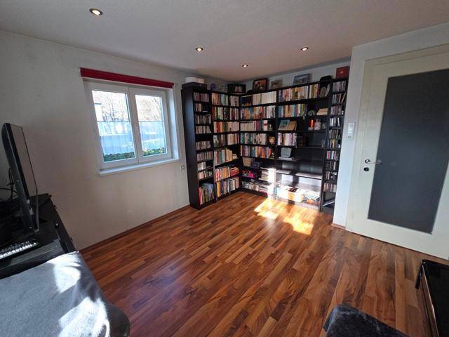 Helles Arbeitszimmer mit großem Bücherregal, Holzboden und Fenster.