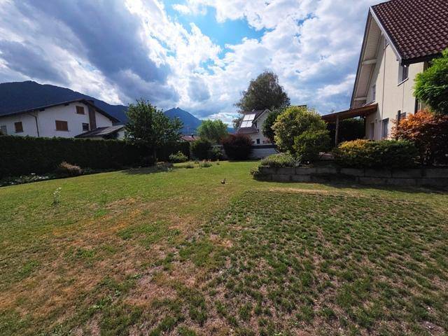 Weitläufiger Gartenbereich mit Rasen und seitlichem Blick auf das Haus sowie die Berglandschaft.
