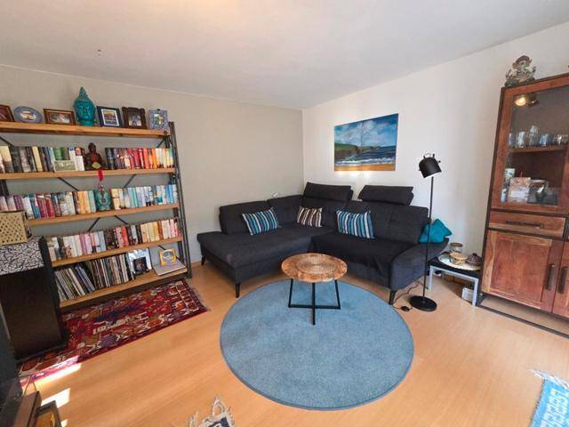 Wohnzimmer mit Ecksofa, großem Bücherregal und Holzboden.