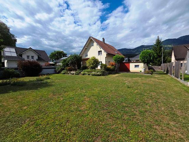Geräumiger Garten mit Rasenfläche vor einem Einfamilienhaus und Bergblick im Hintergrund.