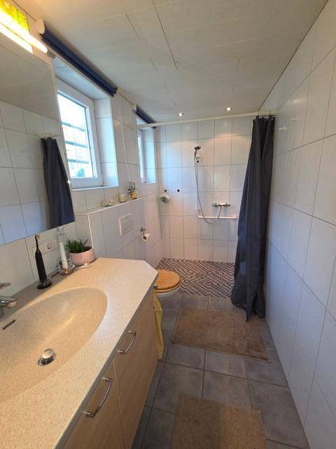 Helles Badezimmer mit großer Dusche, weißen Fliesen und Fenster für Tageslicht.