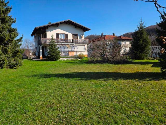 Großer Gartenbereich mit Rasen und Bäumen, der das Wohnhaus mit Balkon und Wintergarten umgibt.