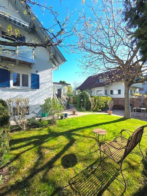 Grüner Garten mit Rasenfläche und einem Baum, im Hintergrund das Wohnhaus mit Balkon.