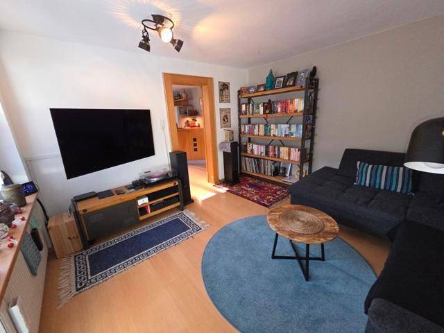 Gemütliches Wohnzimmer mit Sofa, Bücherregal und Fernseher an der Wand.