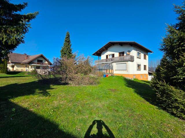 Gartenansicht des Hauses mit Balkon, Wintergarten und angrenzendem Gebäude unter strahlendem Sonnenschein.