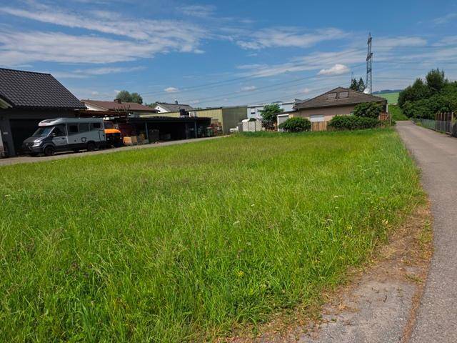 Unbebautes Grundstück mit Rasenfläche, umgeben von Häusern und einem Feldweg.