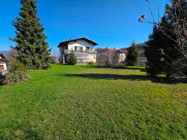 Sonniger Garten mit gepflegtem Rasen und Blick auf das Wohnhaus mit Balkon und Wintergarten.