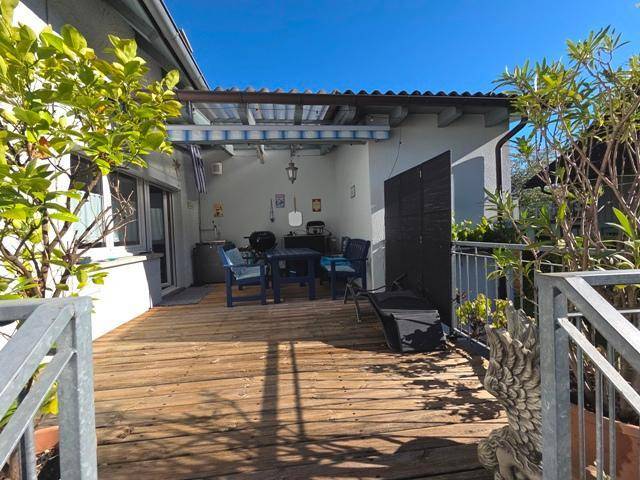 Überdachte Holzterrasse mit Grillbereich und Sitzgelegenheiten, ideal für entspannte Stunden im Freien.
