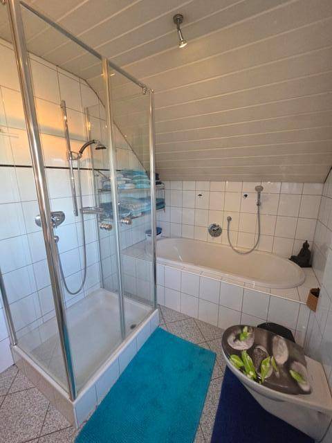Badezimmer im Dachgeschoss mit Badewanne, Duschkabine und weißen Wandfliesen.