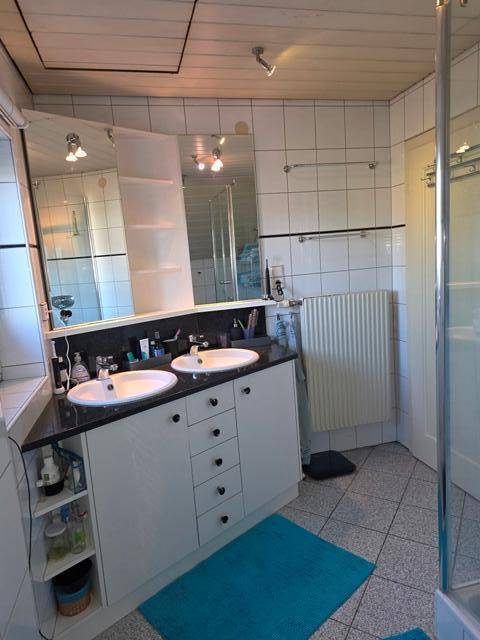 Modernes Badezimmer mit Doppelwaschbecken, Spiegelschrank und Heizkörper.