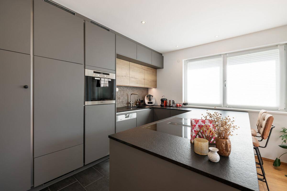 Elegante, moderne Küche mit grauen Schränken, integrierten Geräten und großem Fenster.