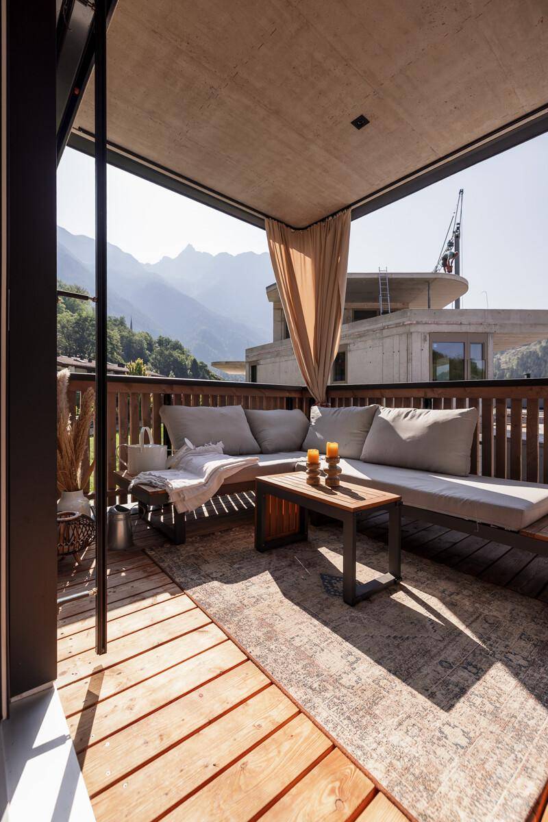 Sonniger Balkon mit Holzboden, bequemen Loungemöbeln und beeindruckendem Bergblick.