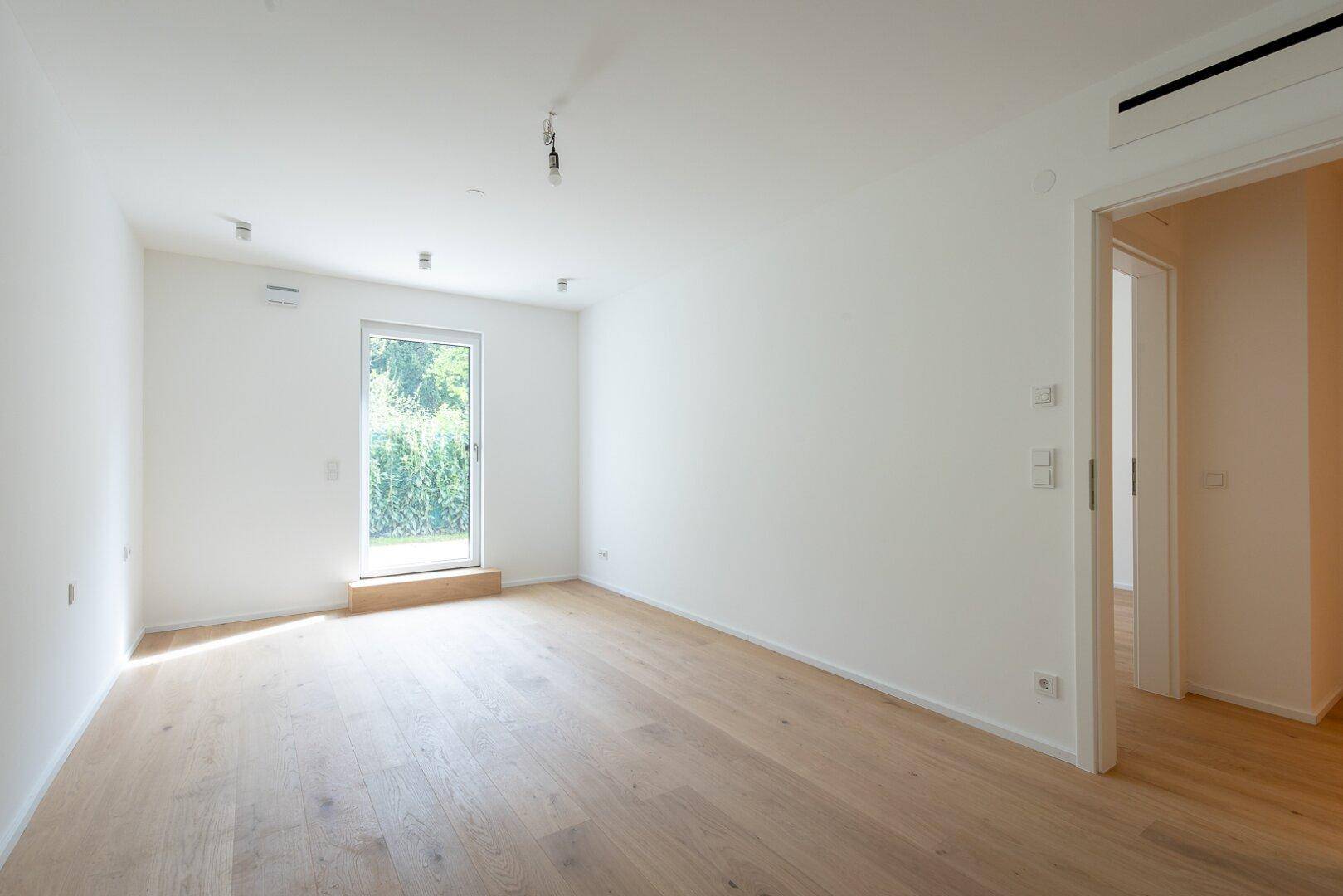 Lichtdurchfluteter, unmöblierter Raum mit Holzboden und direktem Gartenzugang.