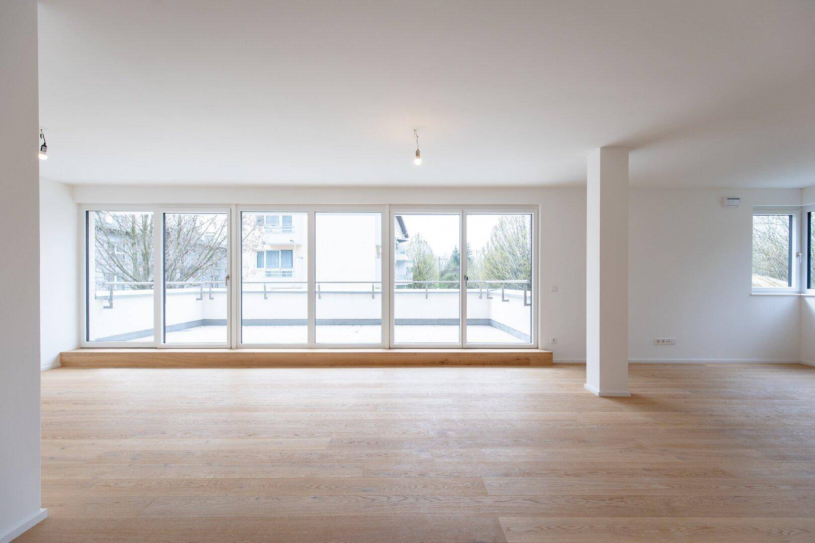 Heller Wohnbereich mit breiter Fensterfront und Zugang zu einer großzügigen Terrasse oder Balkon.
