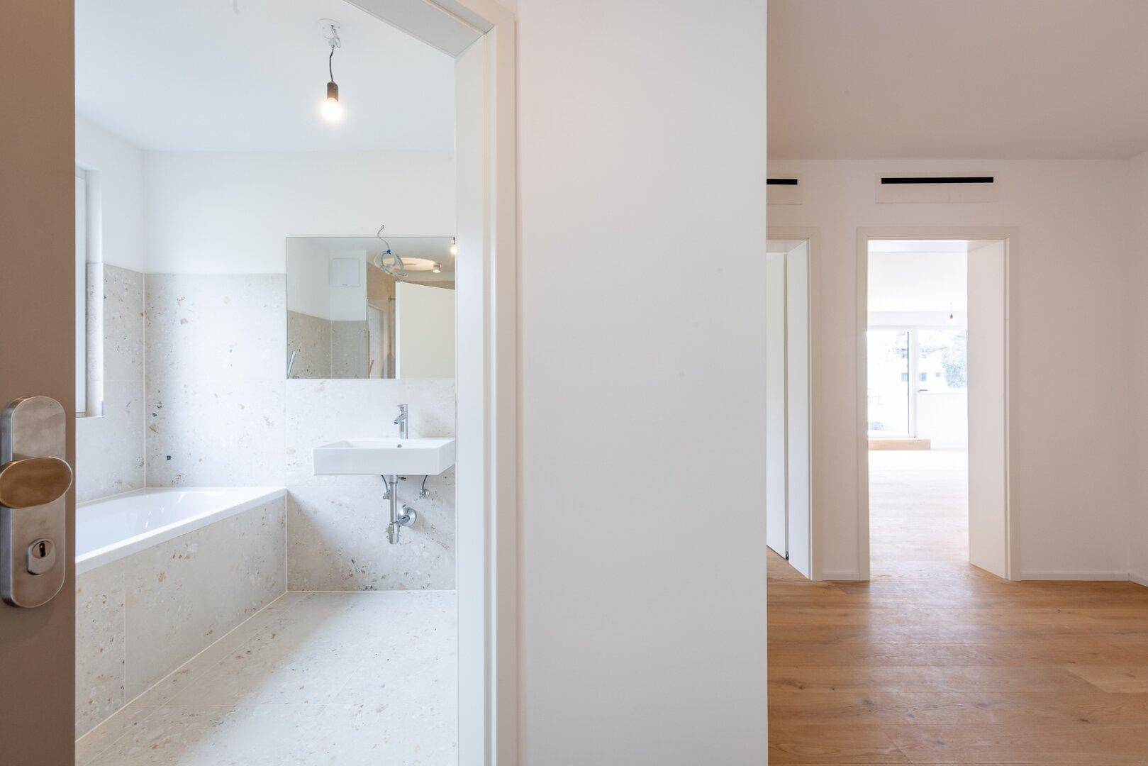 Eingangsbereich zu einem modernen Badezimmer mit Badewanne und hellen Fliesen.