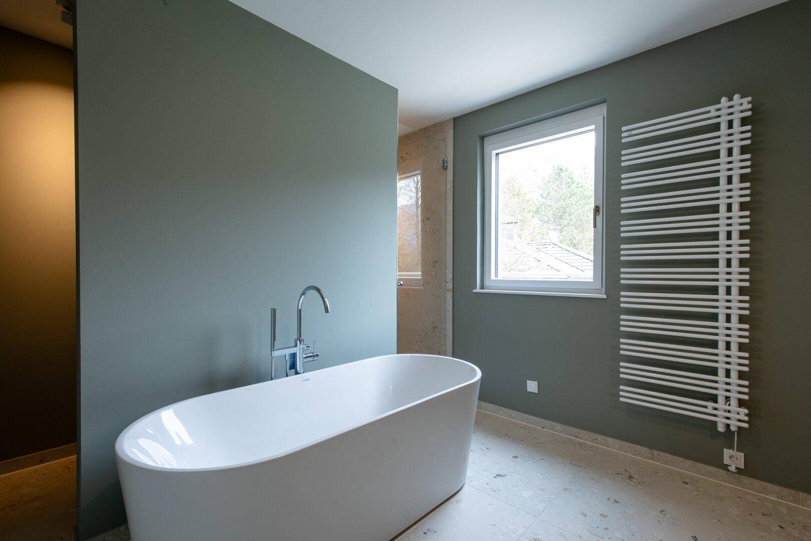 Modernes Badezimmer mit freistehender Badewanne, beheiztem Handtuchhalter und Fenster.
