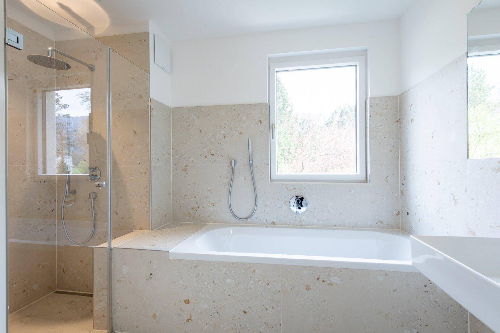 Modernes Badezimmer mit Badewanne, ebenerdiger Dusche und Fenster, ausgestattet mit hellen Fliesen.