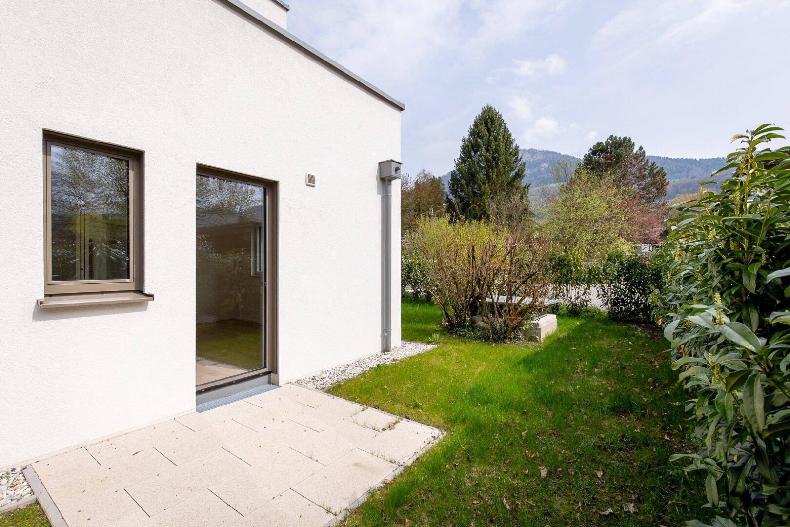Gartenbereich mit Rasenfläche, Sträuchern und Zugang zum Haus in ländlicher Umgebung.