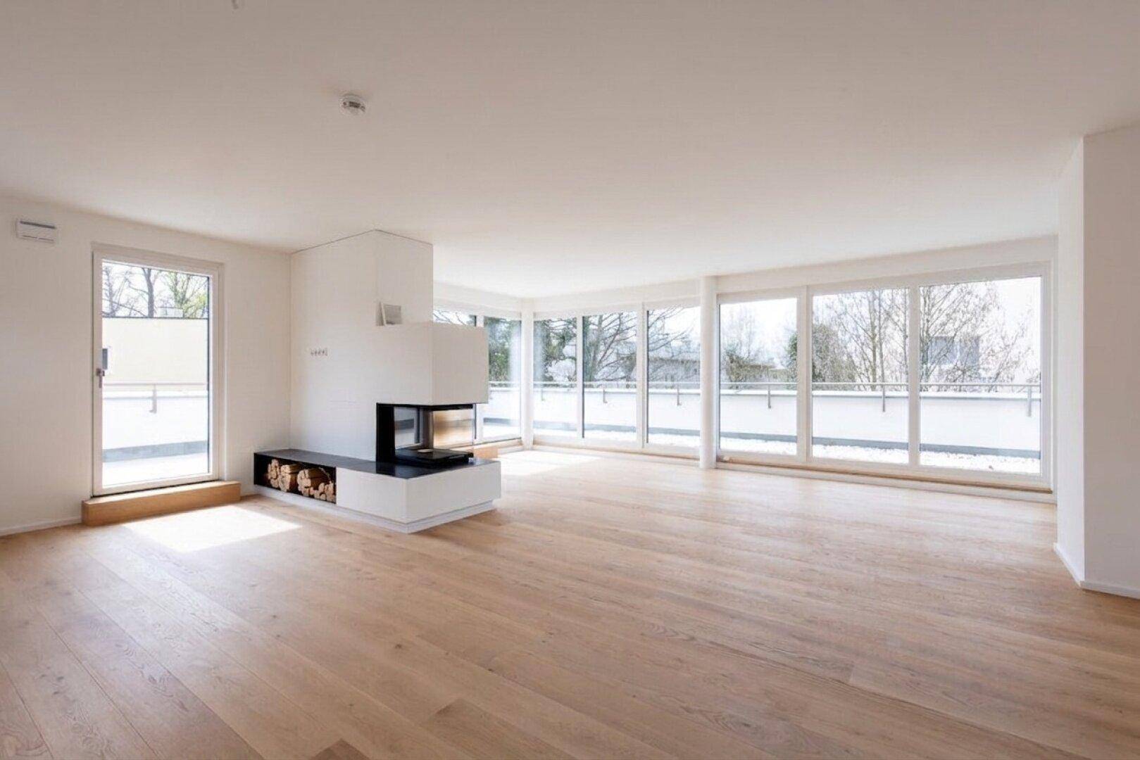 Geräumiges Wohnzimmer mit Kamin, großen Fensterfronten und Zugang zur Terrasse.