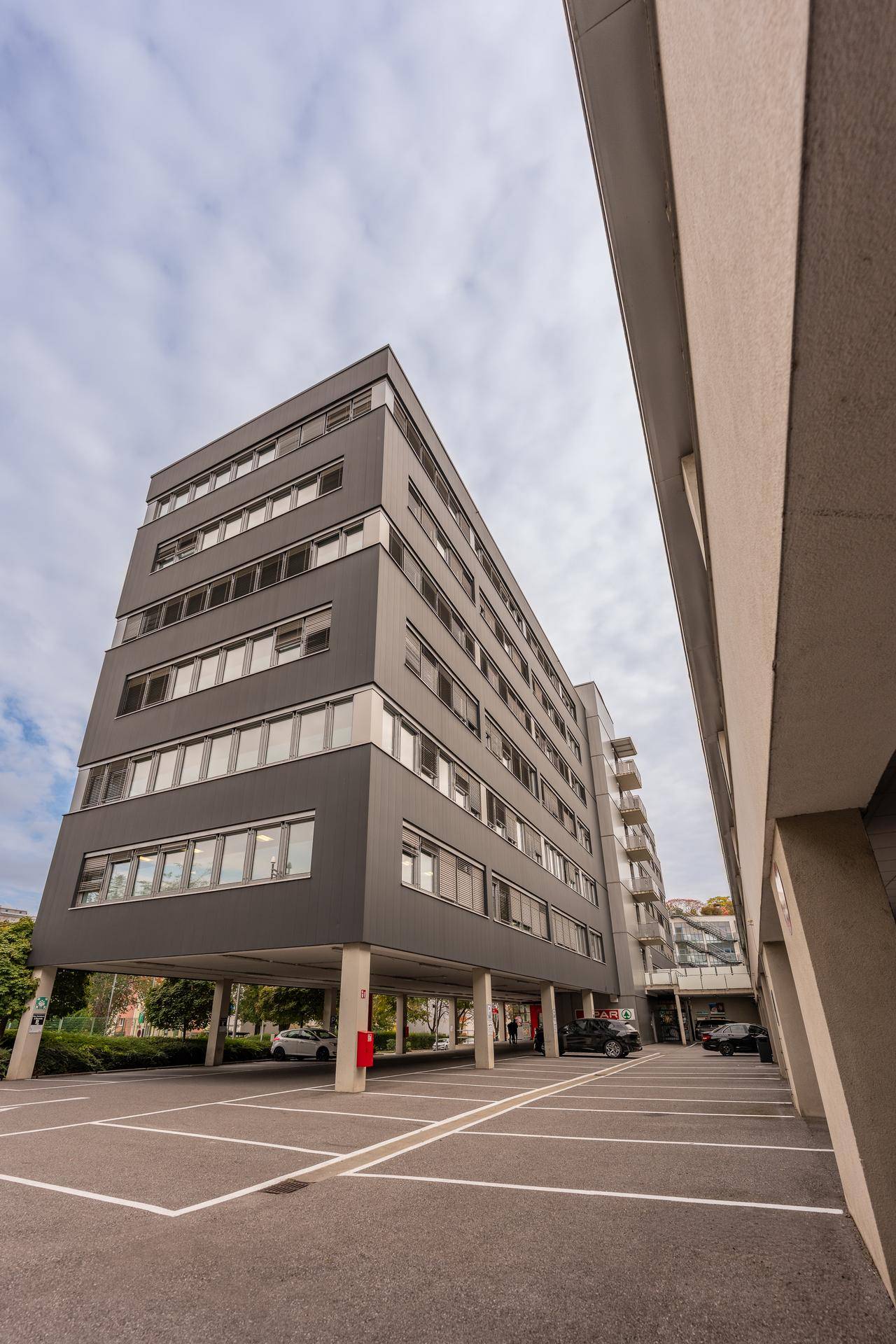Moderne Gebäudearchitektur mit überdachten Parkplätzen im Erdgeschoss und klarem Himmel.