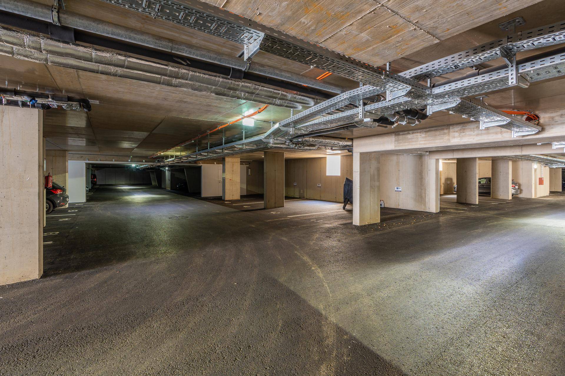Weitläufige Tiefgarage mit Betonstützen und offener Deckeninstallation, bietet ausreichend Parkraum.