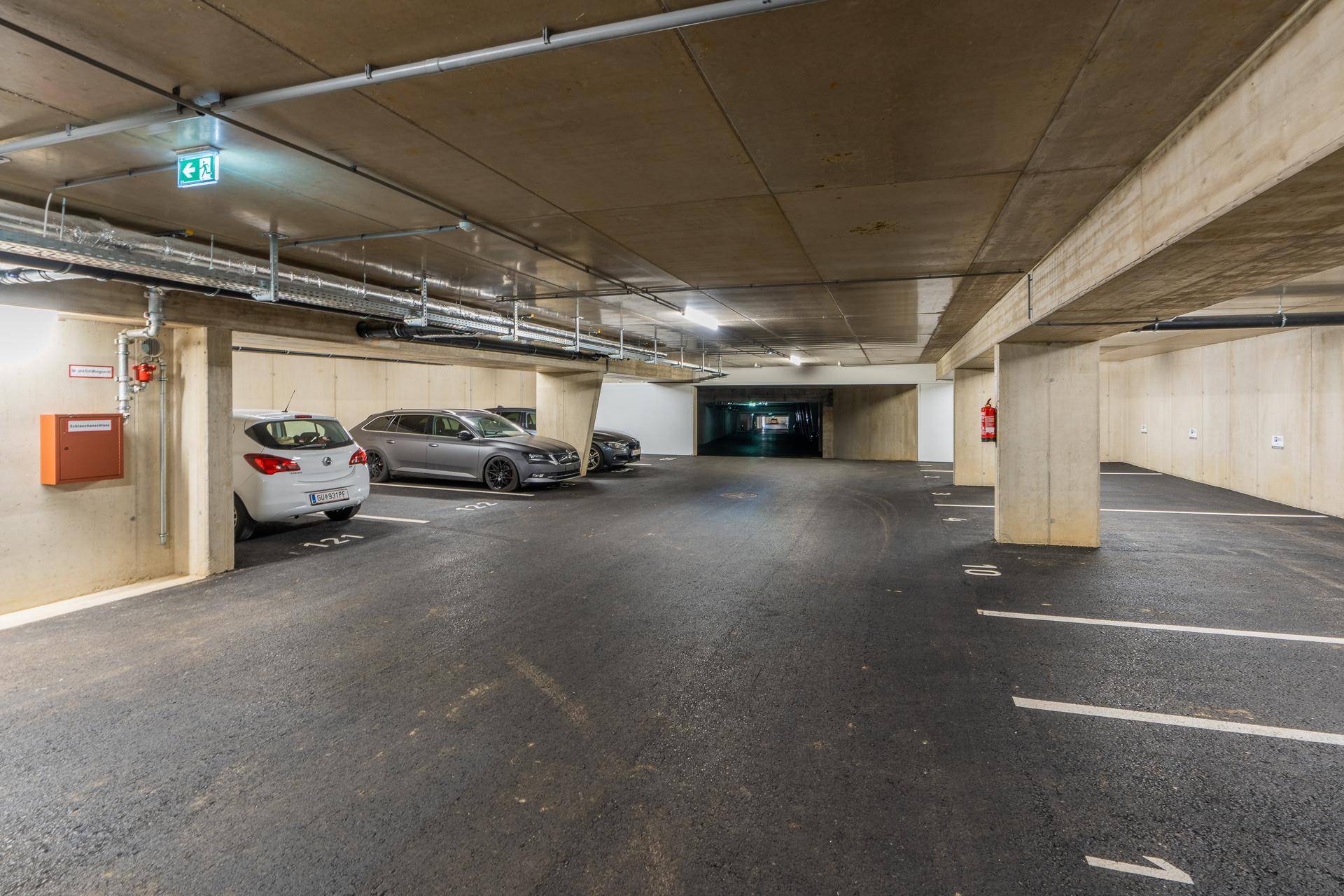 Geräumige Tiefgarage mit markierten Stellplätzen, Betonpfeilern und sichtbaren Versorgungsleitungen an der Decke.