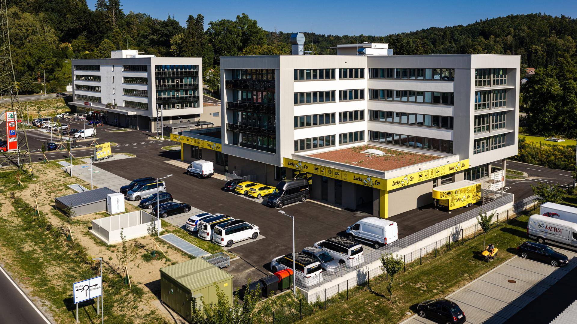 Zwei moderne Geschäftsgebäude mit Parkplätzen und umliegender grüner Landschaft.