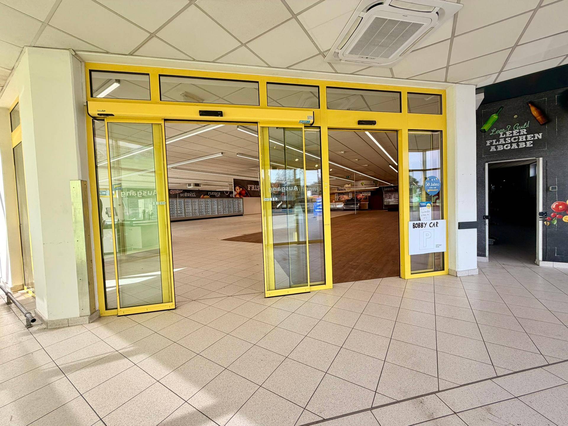 Eingangsbereich eines Supermarktes mit automatischen Schiebetüren und Blick in den Verkaufsraum.