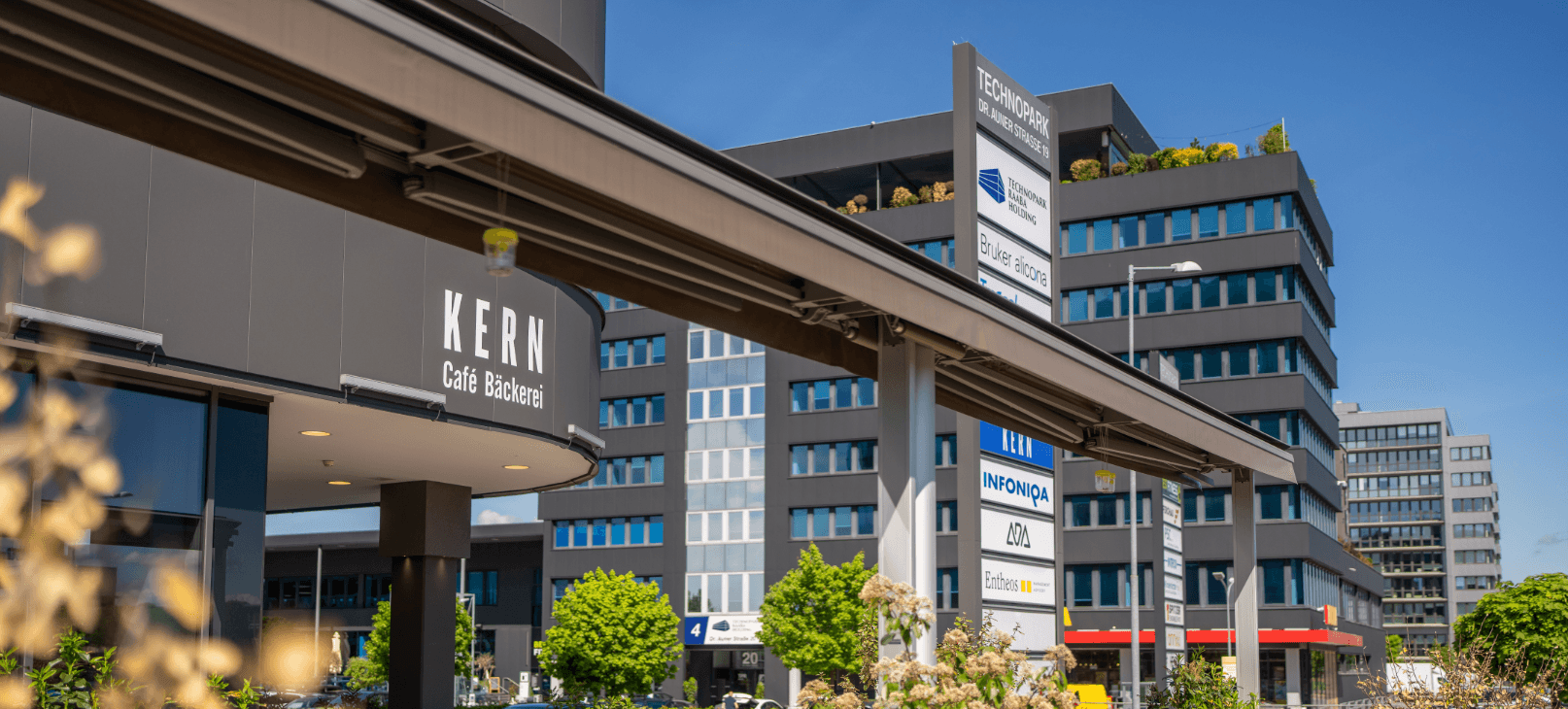 Fassade eines modernen Büro- und Geschäftsgebäudes mit verschiedenen Firmenlogos und Geschäften im Erdgeschoss.