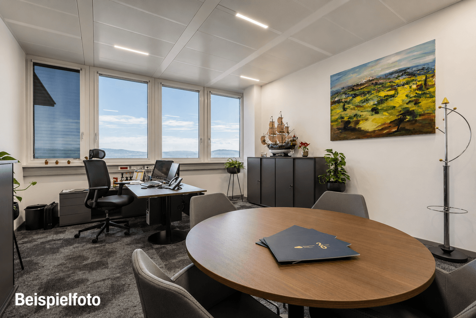 Helles Einzelbüro mit großzügigen Fenstern, modernem Schreibtisch und einem runden Besprechungstisch.