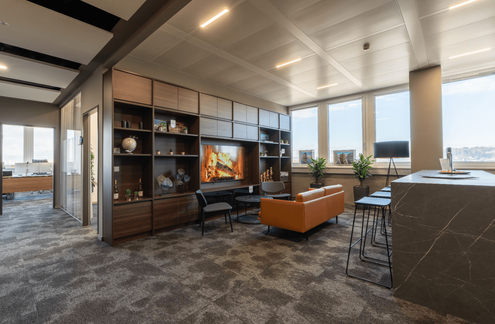 Moderner Loungebereich mit bequemen Sofas, Medieneinheit und Bartheke in einem Bürogebäude.