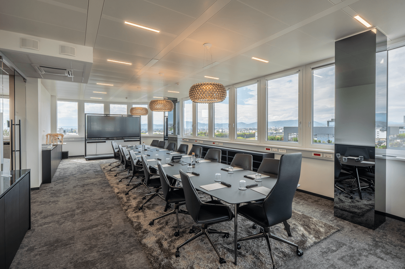 Großer Konferenzraum mit modernem Design, langen Tischen und Panoramablick durch die Fenster.