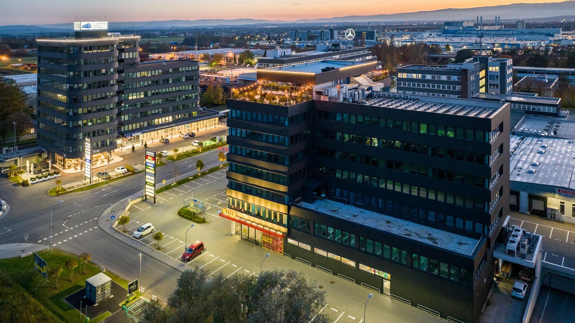 Luftaufnahme eines modernen Bürokomplexes bei Sonnenuntergang mit beleuchteten Außenbereichen.