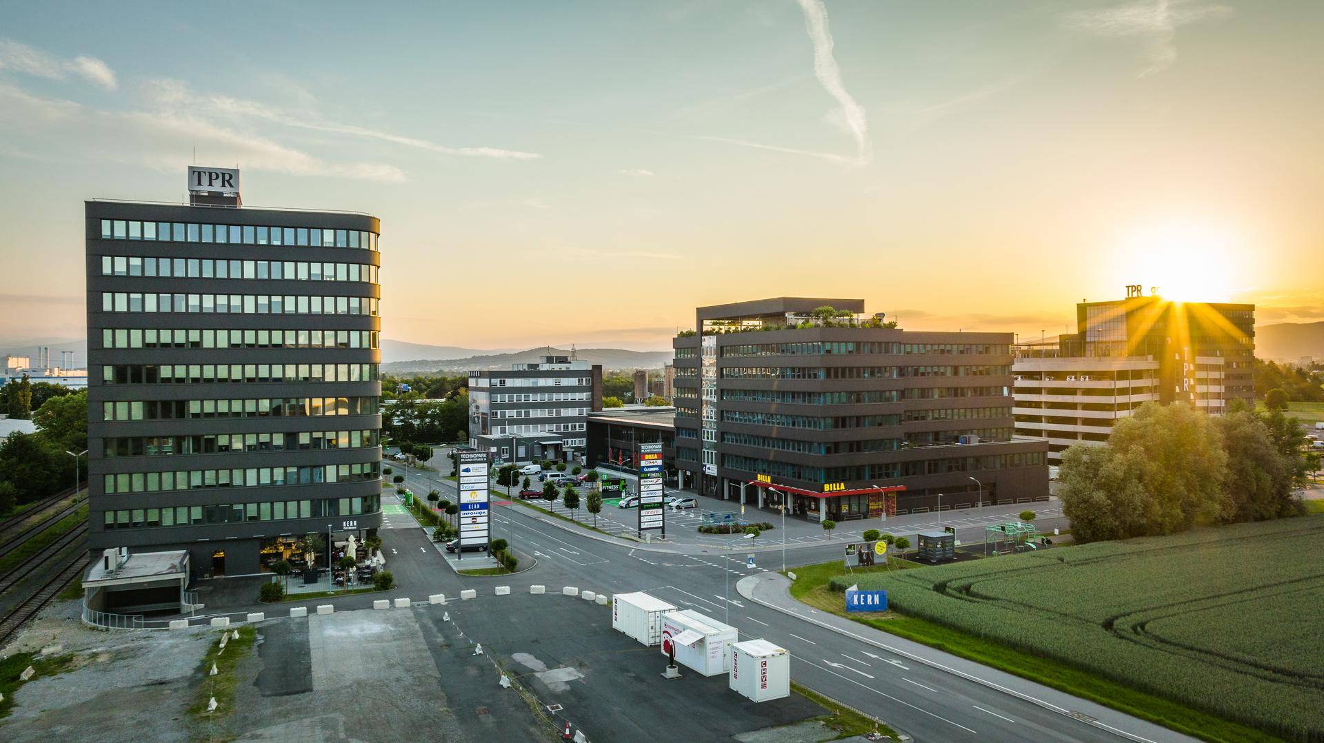 Panoramablick auf einen Gewerbepark bei Sonnenuntergang mit modernen Bürogebäuden, Straßen und angrenzenden Feldern.