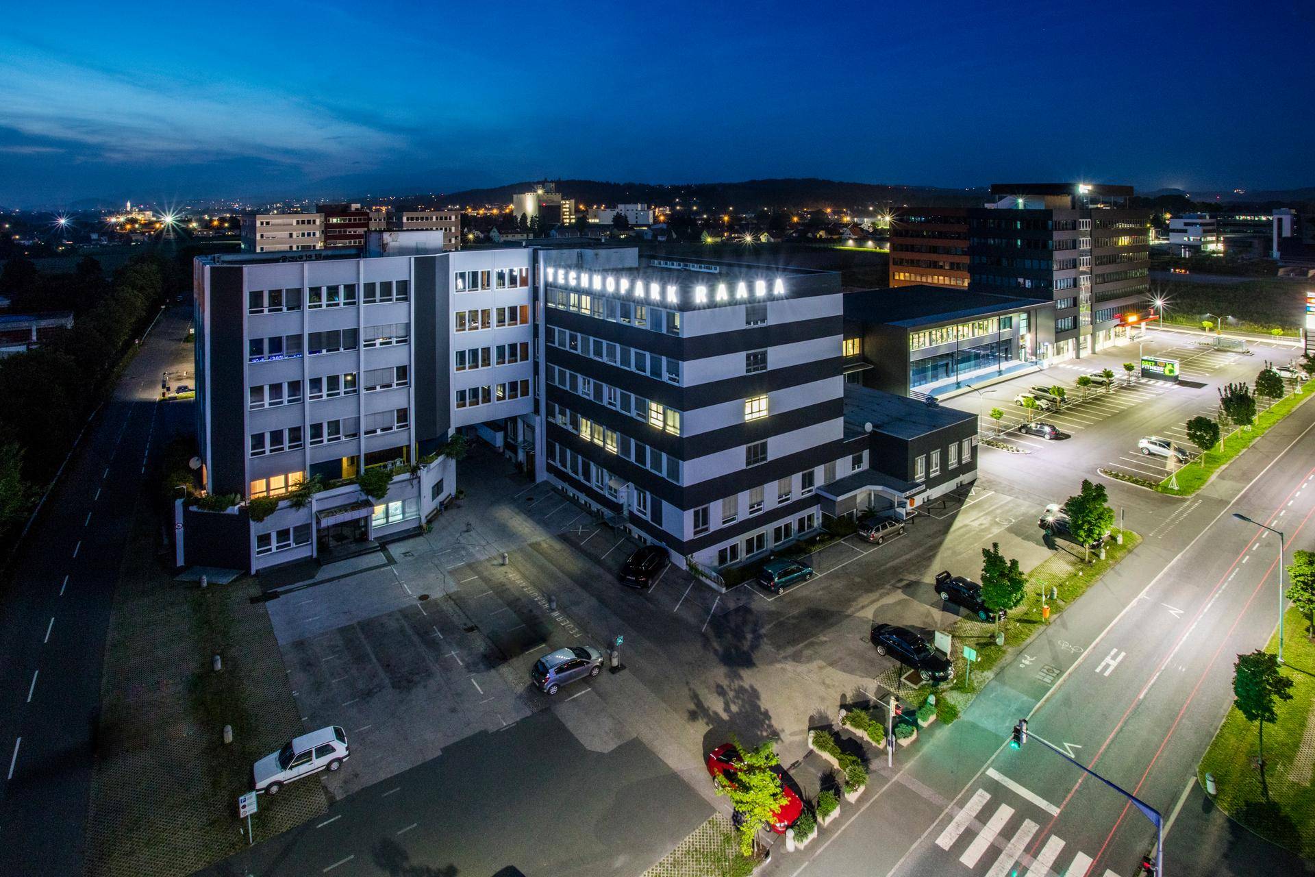 Nachtaufnahme des Technopark Raaba Gebäudekomplexes mit beleuchteten Straßen und Parkplätzen.