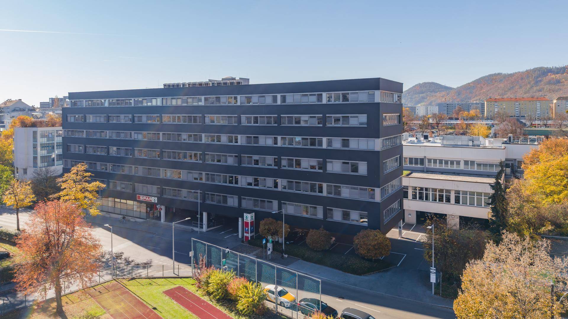 Blick auf die moderne Fassade eines Bürogebäudes mit Einzelhandelsflächen im Erdgeschoss und umliegender Stadtlandschaft.
