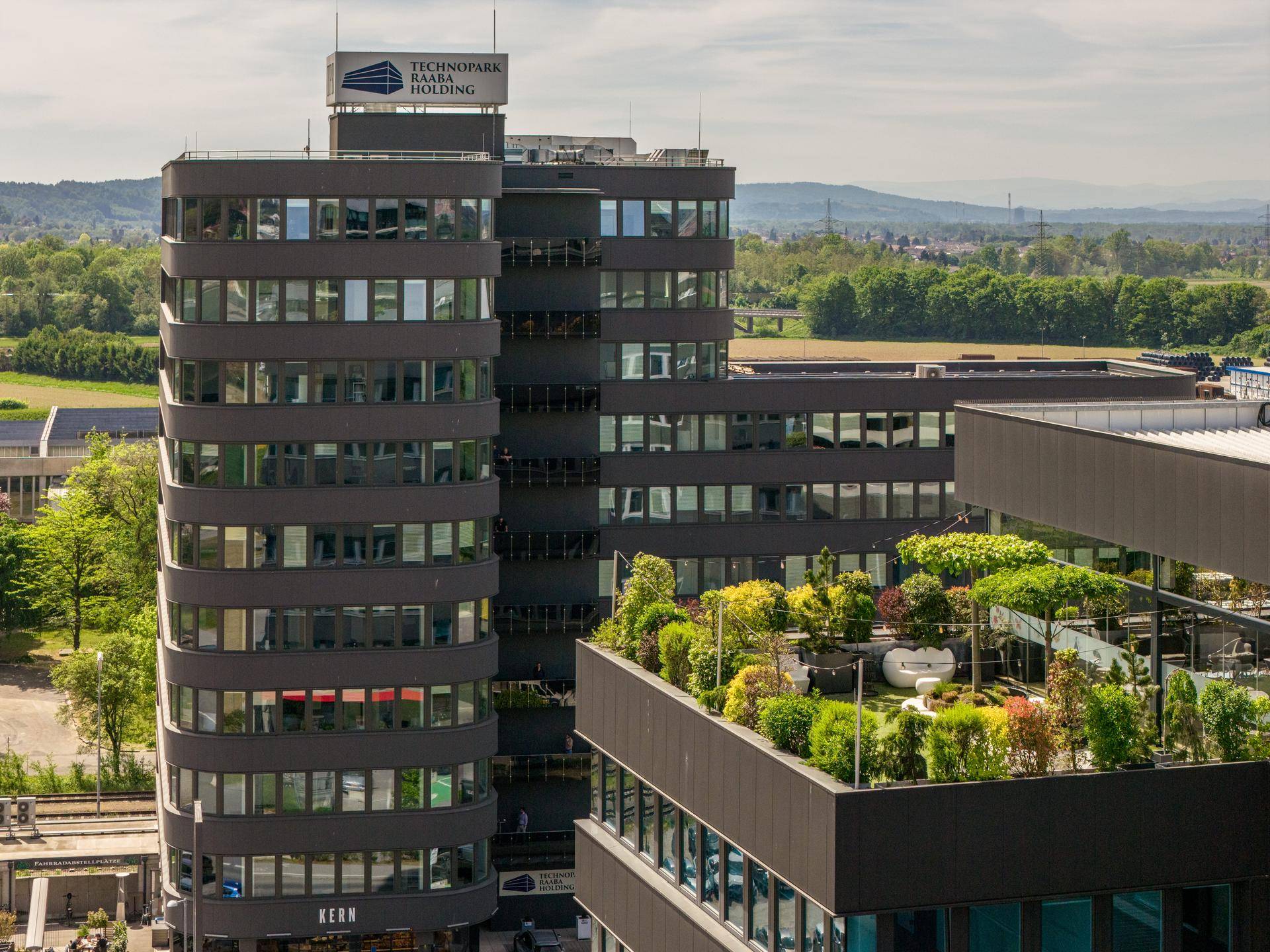 Dachterrasse mit üppiger Bepflanzung und Sitzgelegenheiten auf dem modernen Bürogebäude.