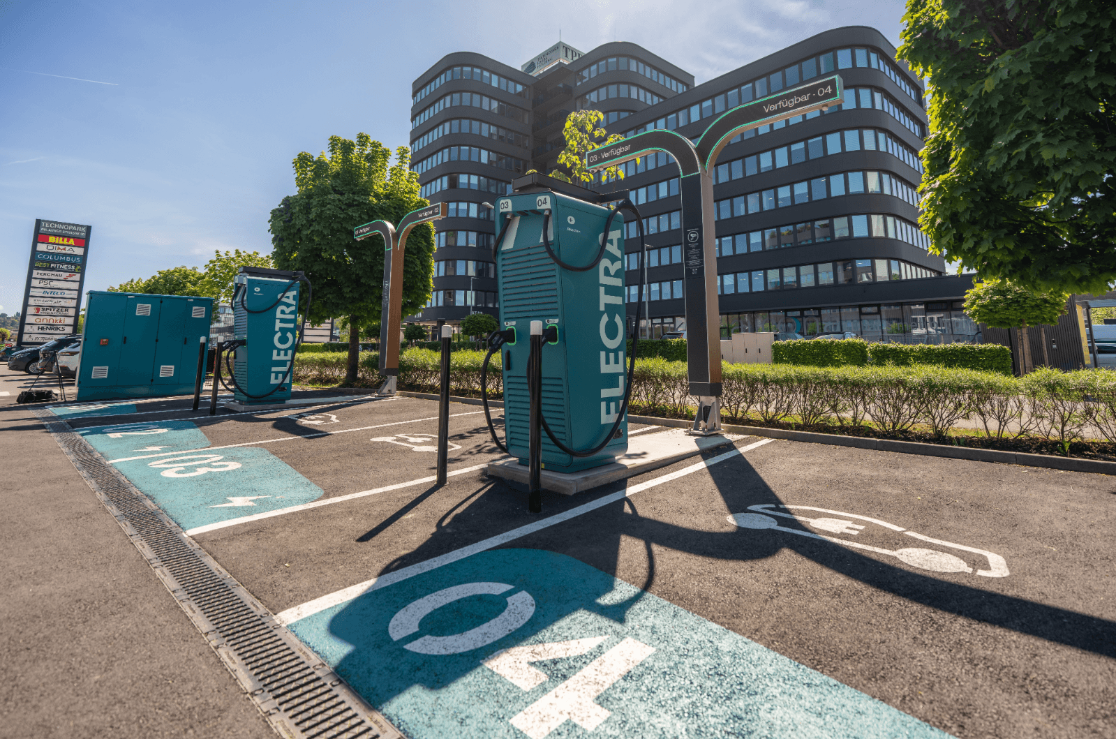 Moderne Ladestationen für Elektrofahrzeuge vor einem Bürogebäude unter blauem Himmel.