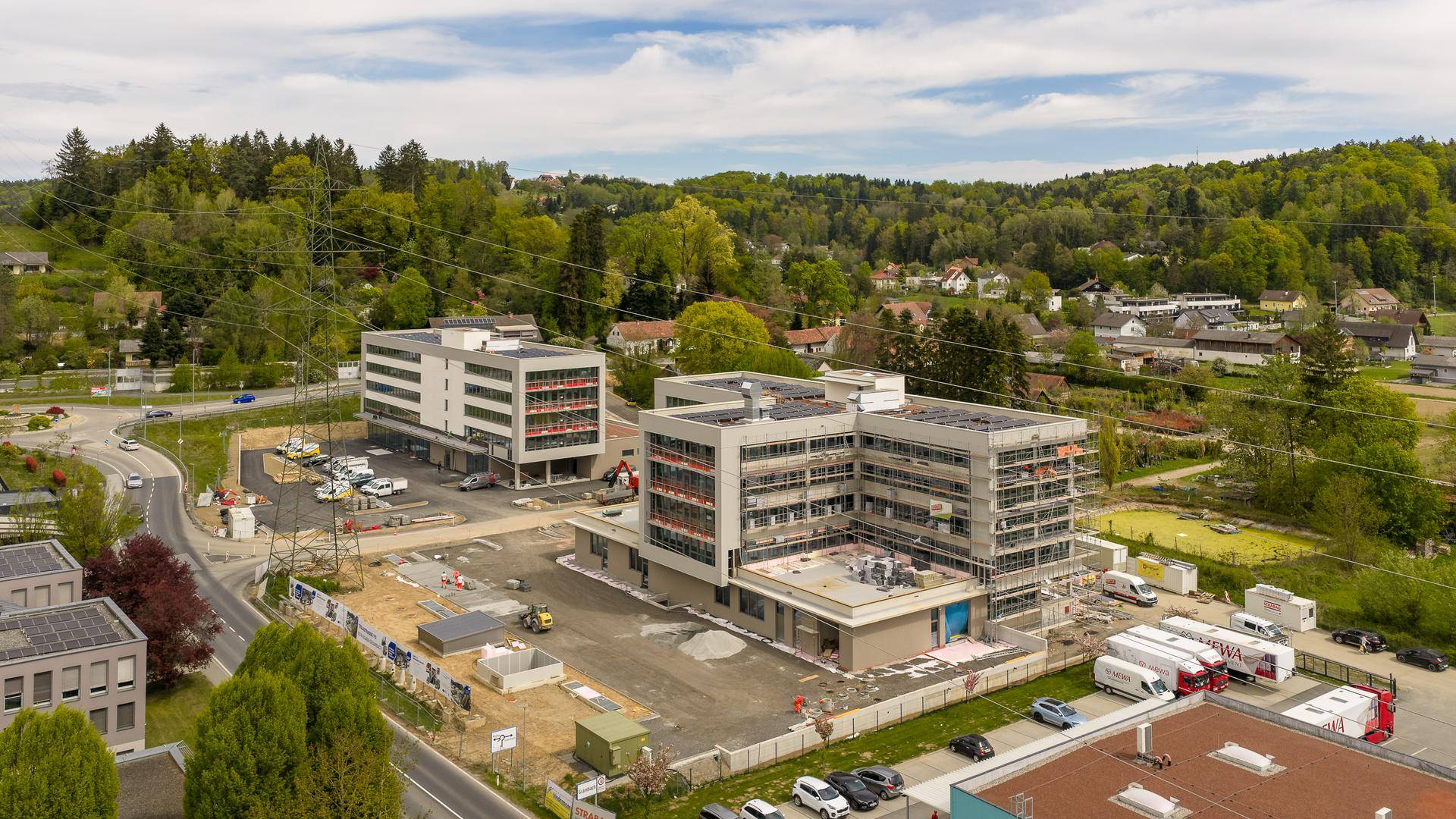 Luftaufnahme einer Baustelle mit zwei modernen Neubauten und umliegender grüner Landschaft.