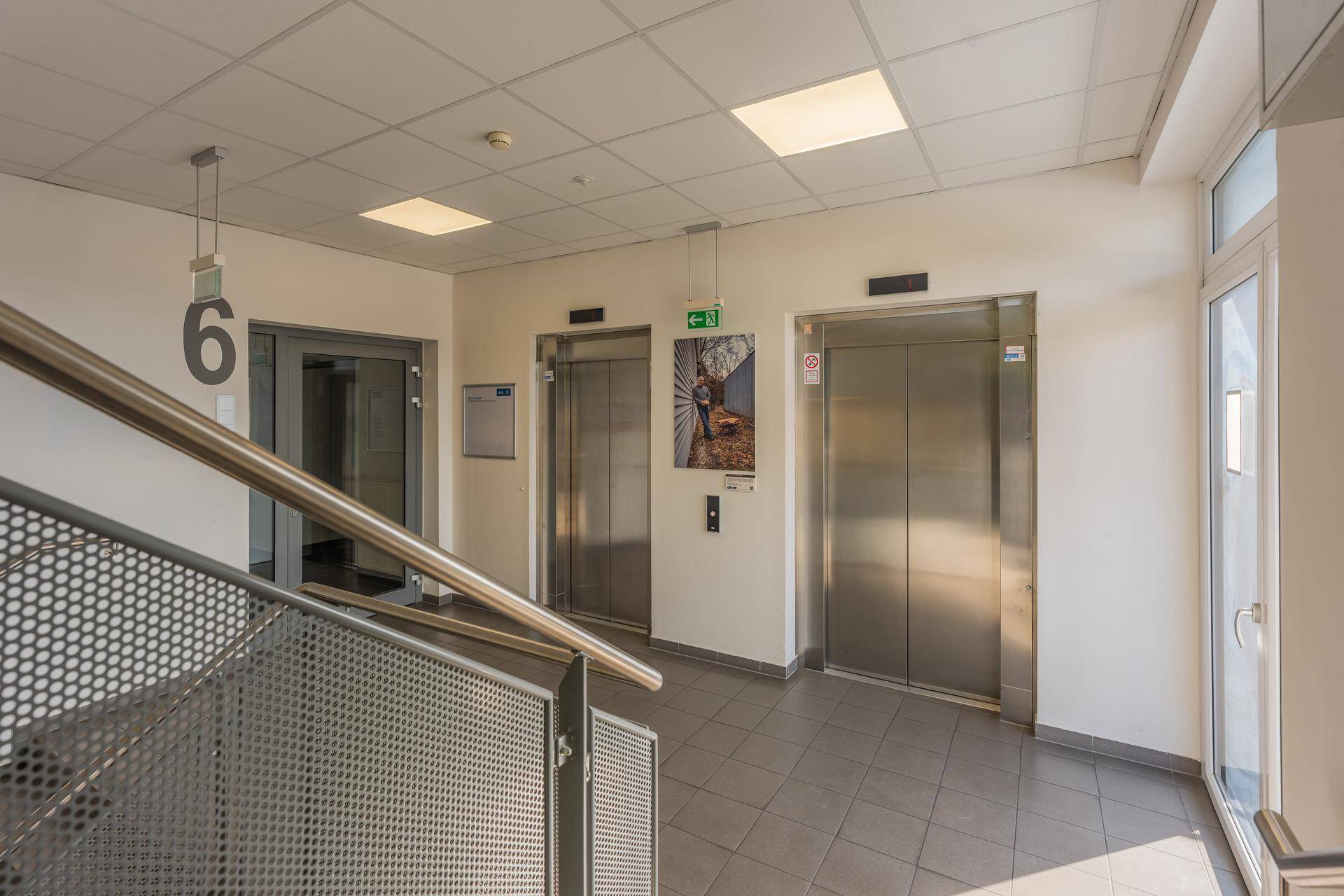 Heller Eingangsbereich mit zwei modernen Aufzügen, einer Treppe und Fliesenboden.