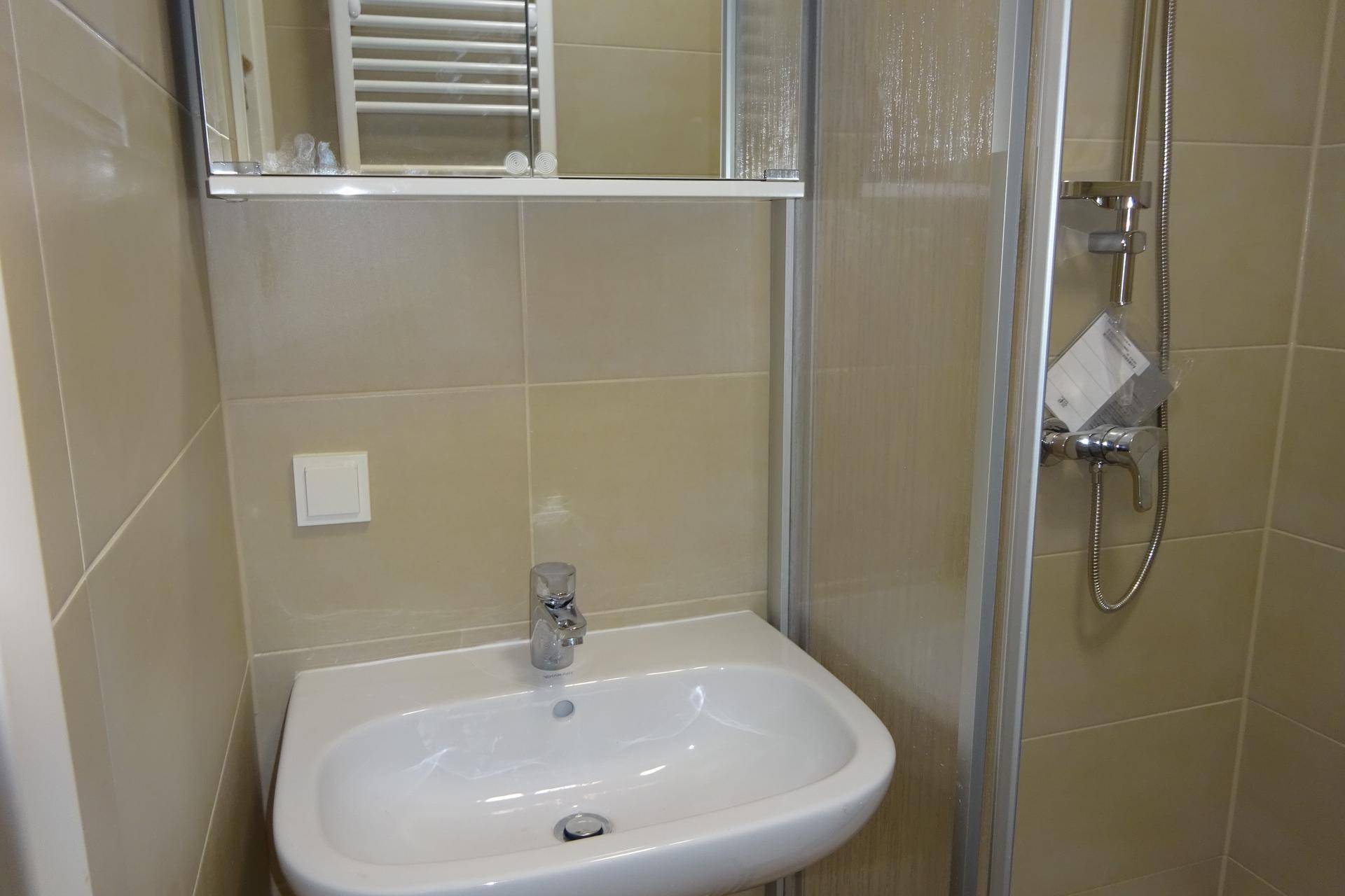 Funktionales Badezimmer mit Waschbecken, Spiegelschrank und Duschkabine, alles in hellen Tönen gehalten.