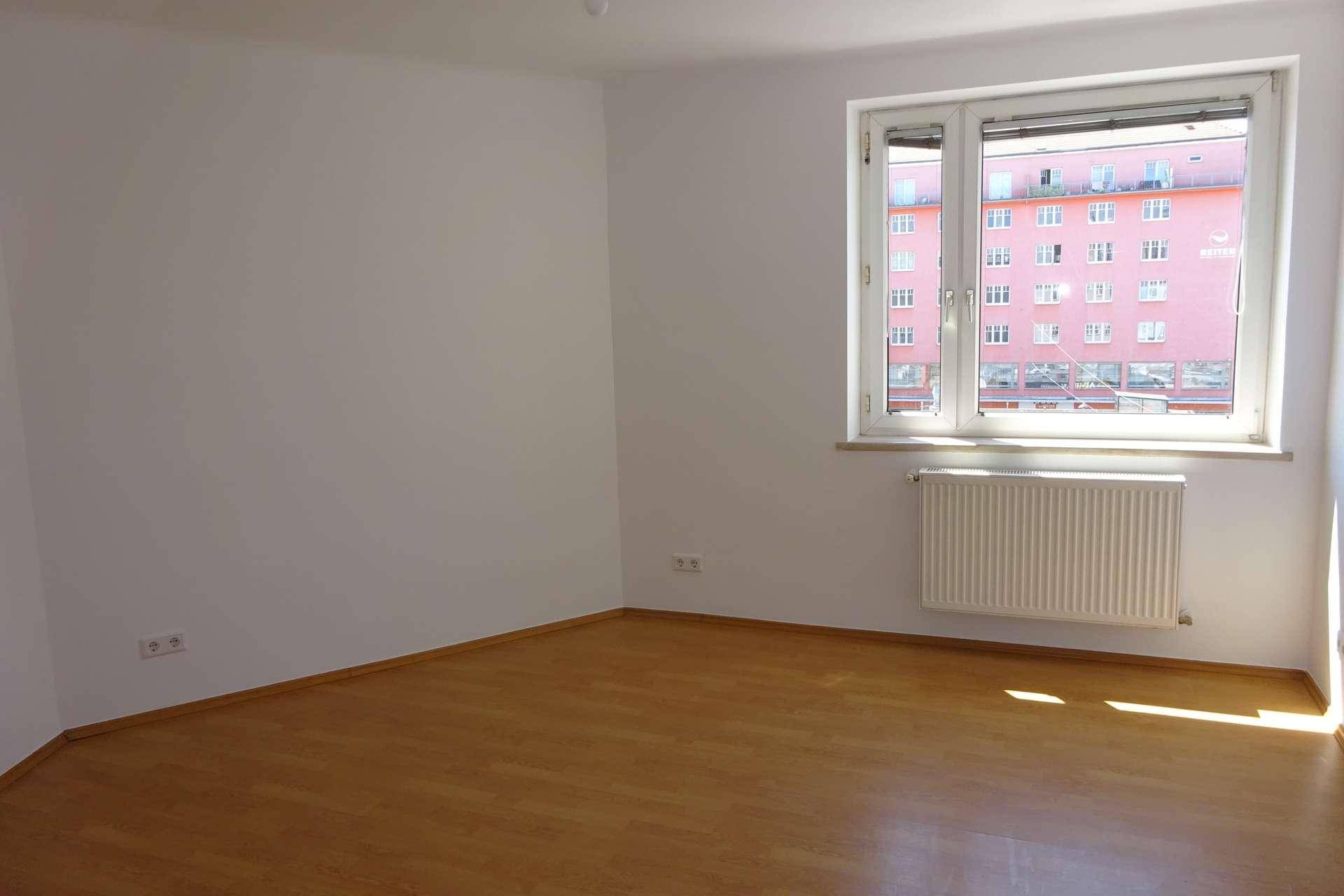 Geräumiges, helles Zimmer mit Holzboden und einem großen Fenster mit Blick auf die Stadt.