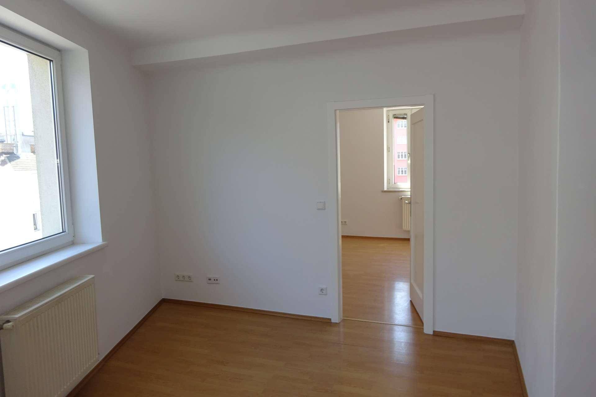 Heller Raum mit Parkettboden und Zugang zu einem weiteren Zimmer, ideal für flexibles Wohnen.