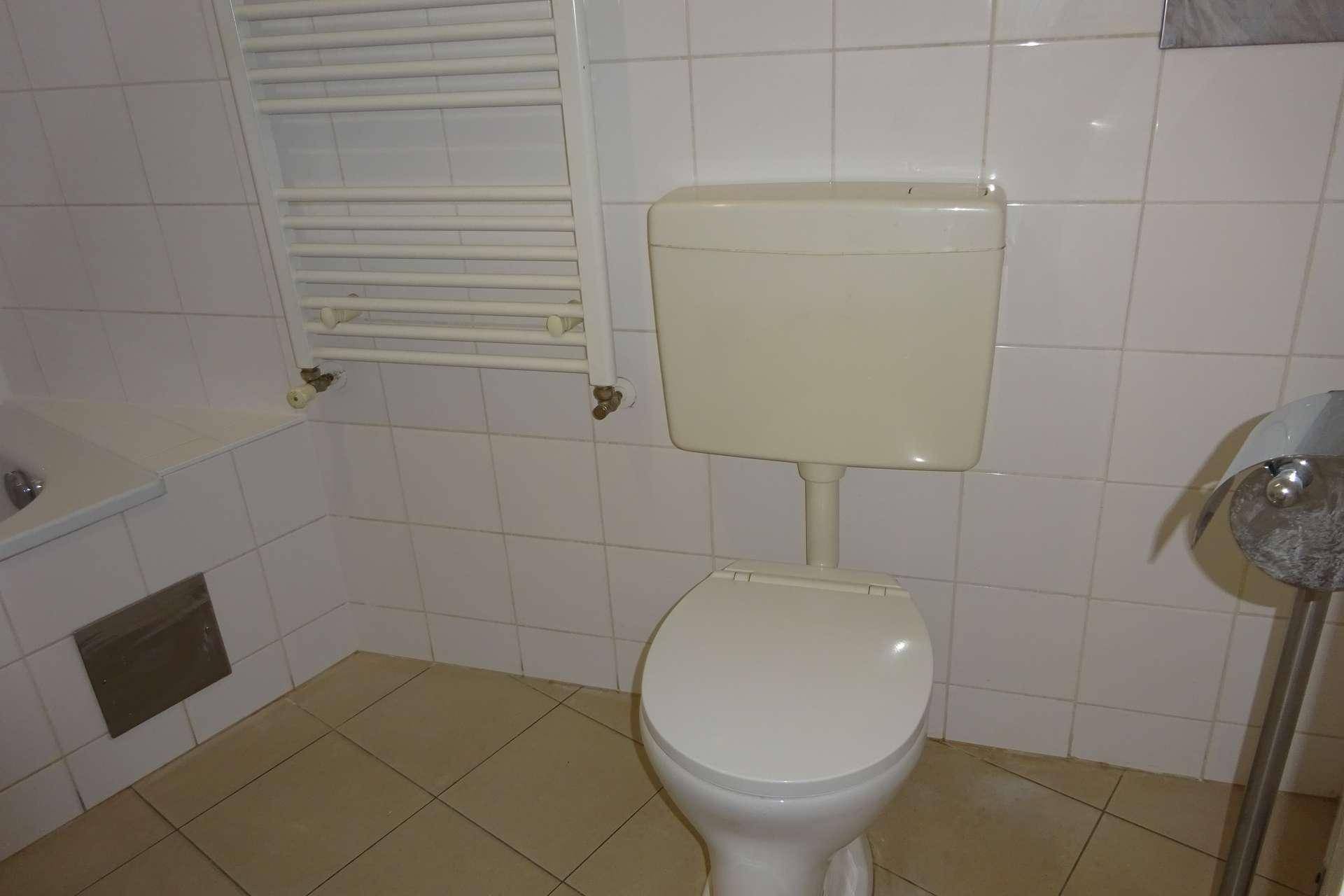 Toilette in einem gefliesten Badezimmer mit klassischem Spülkasten und Handtuchheizkörper.