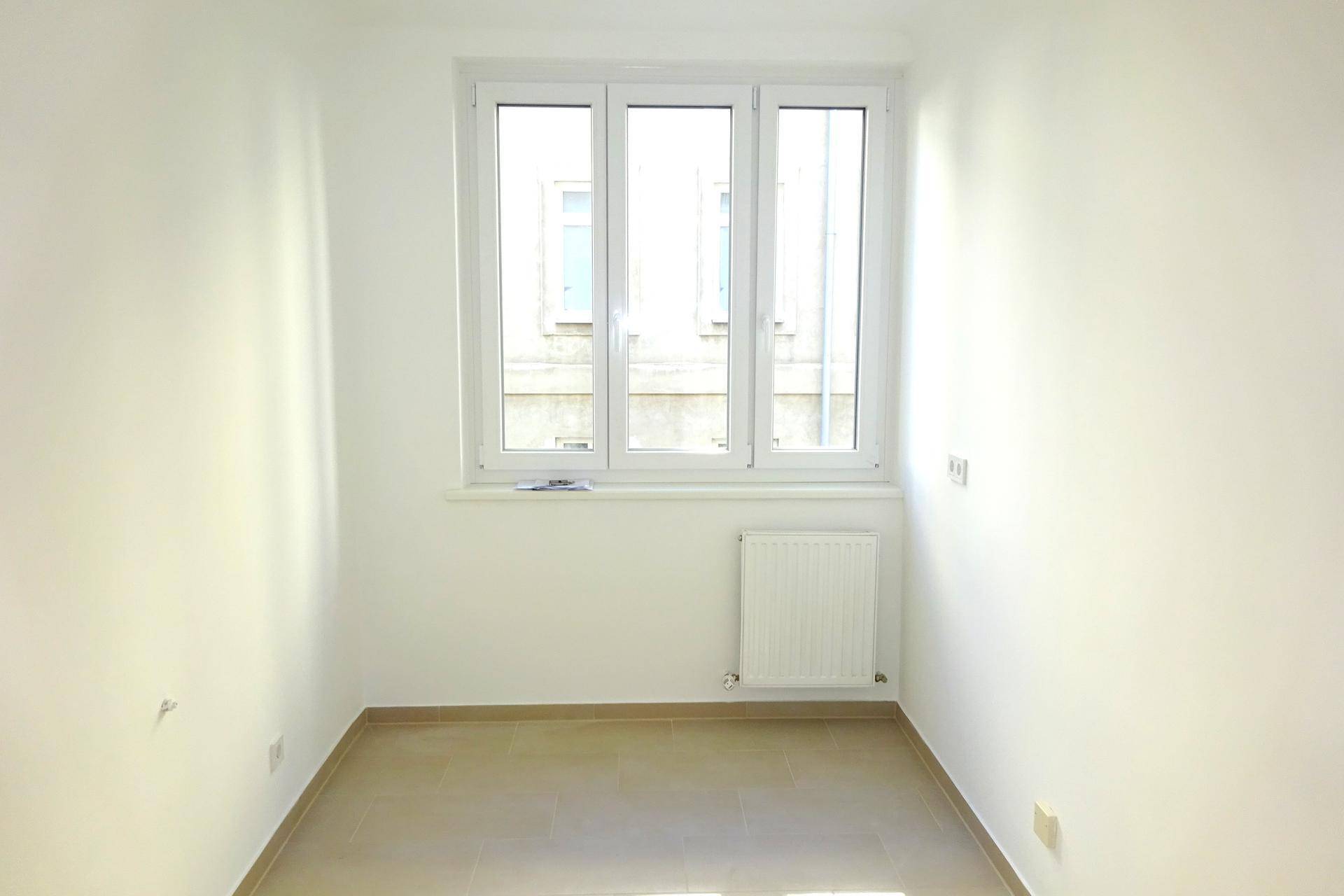 Helles, leeres Zimmer mit Fliesenboden und einem Fenster, das den Raum mit Licht füllt.