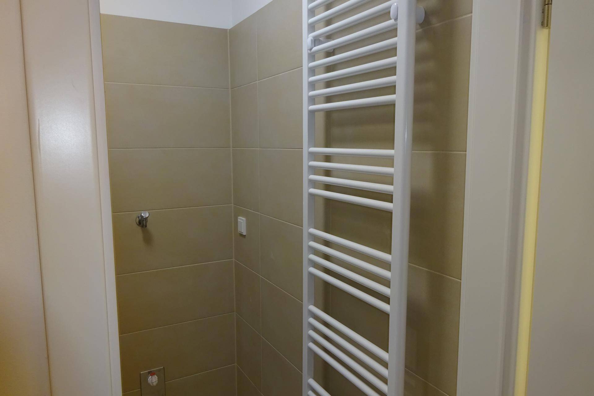 Badezimmerdetail mit einem modernen Handtuchheizkörper und beigefarbenen Wandfliesen.