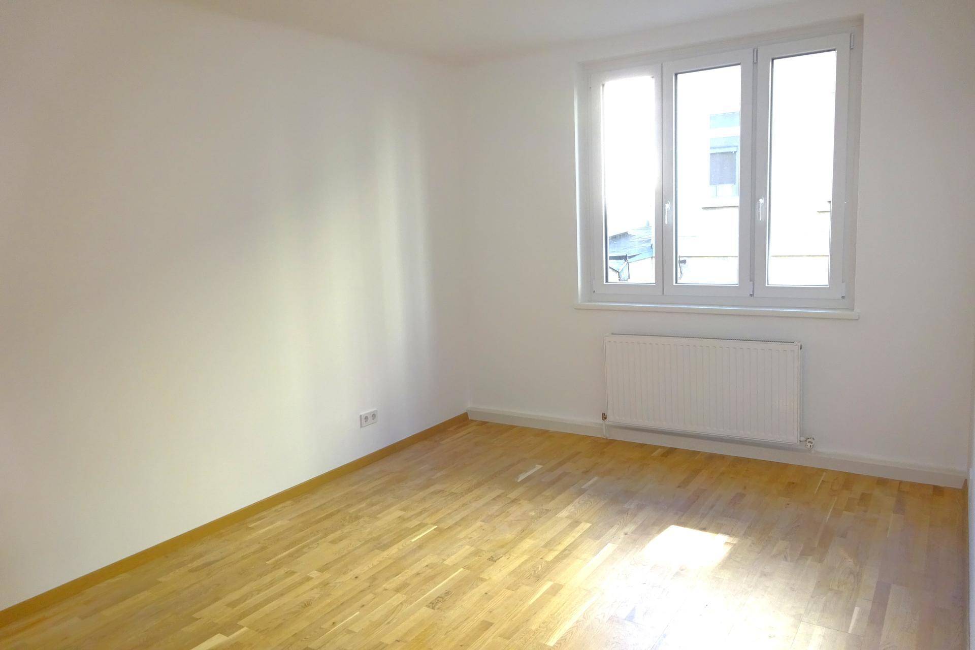 Leeres Schlafzimmer mit hellem Parkettboden und einem Fenster, das den Raum gut belichtet.