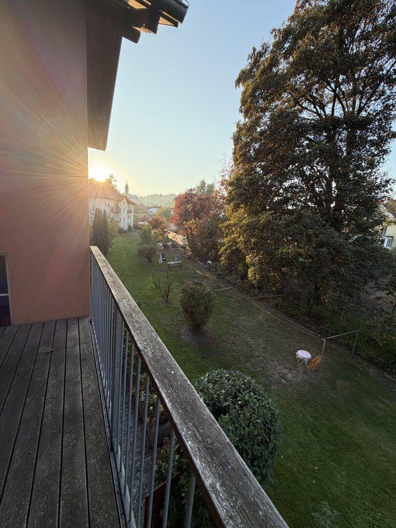 Balkon mit Holzboden und weitem Blick über einen grünen Garten und die Umgebung.