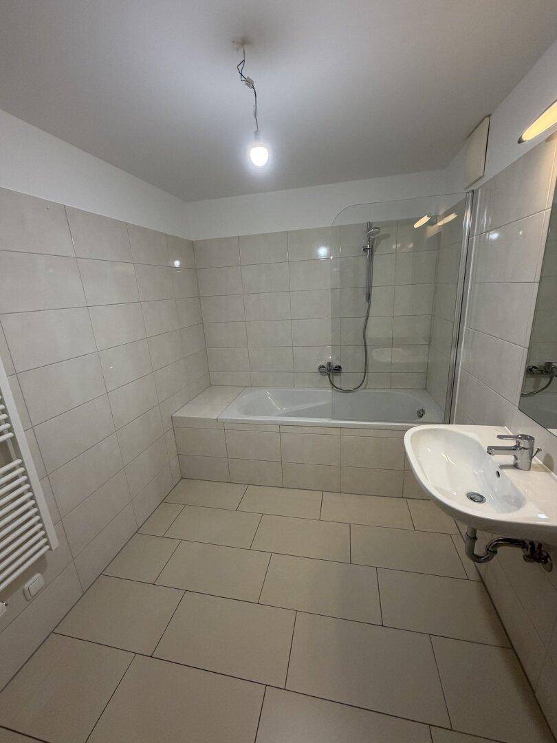 Helles Badezimmer mit Badewanne, Duschabtrennung, Waschbecken und beheiztem Handtuchhalter.
